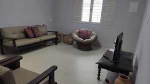 Una sala de estar con sofá, sillón, mesa de centro y televisión.