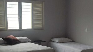 Un dormitorio con dos camas, una ventana con persianas y una mesita de noche.