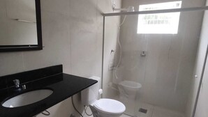 Un baño moderno con lavamanos de superficie negra, inodoro blanco y ducha con mampara de vidrio.