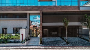 Een modern gebouw met een bordje voor Sunrise Residence. Het heeft een meerlaags gebouw met grote ramen en een hekwerk.