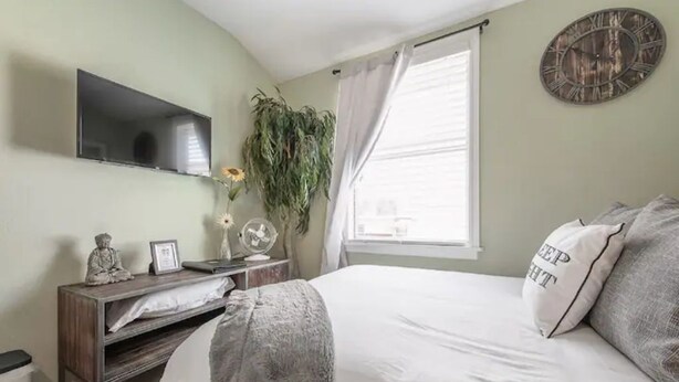 A bedroom with a bed, a bedside table with a lamp, a TV mounted on the wall, and a window with curtains. - Comfy & Cozy Ybor City Studio steps from 7th Ave. #5 (Tampa)