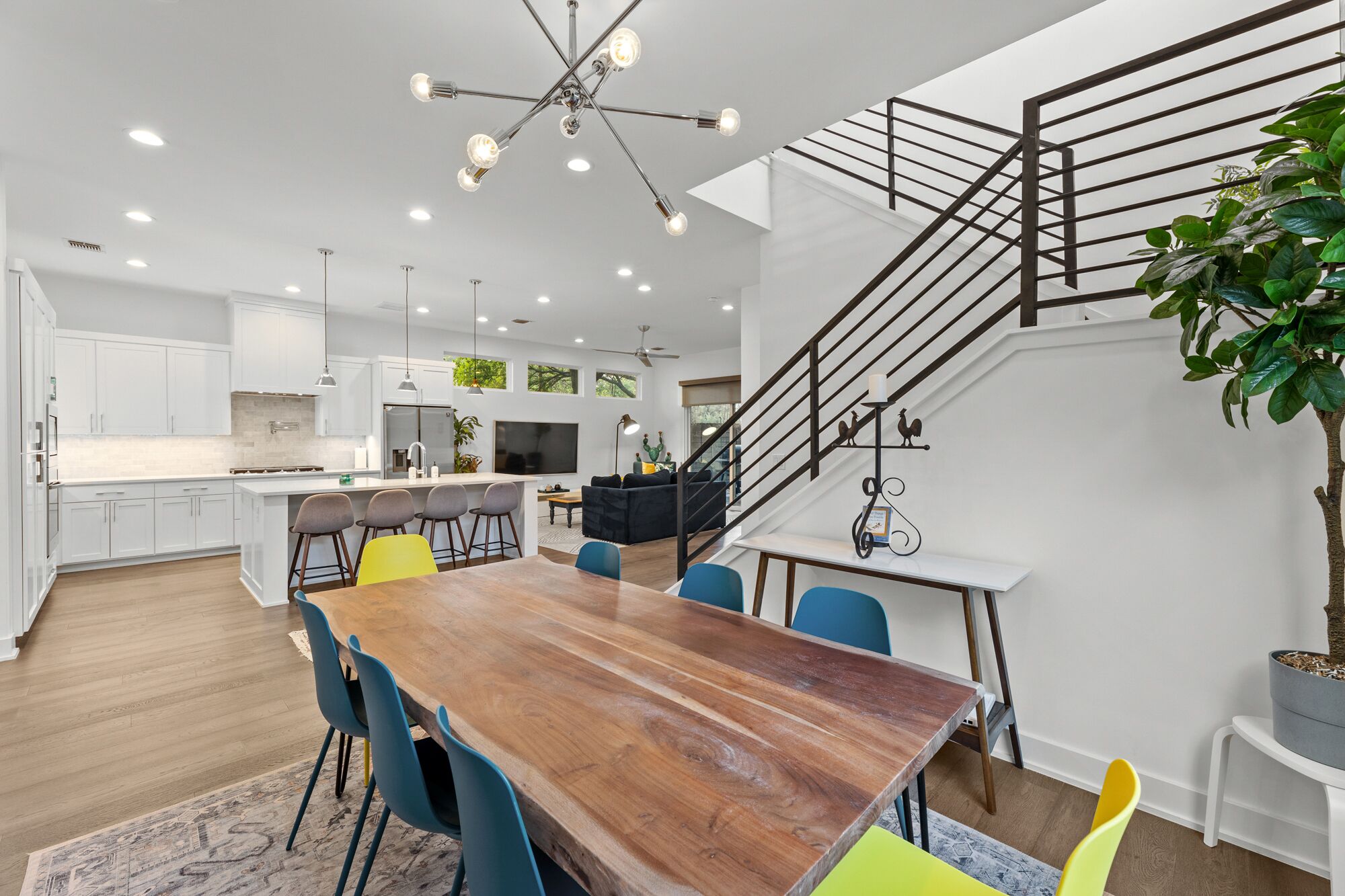 Una cocina moderna con armarios blancos, una isla central y un comedor con una mesa de madera y sillas coloridas.