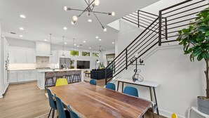 A modern kitchen with white cabinets, a central island, and a dining area with a wooden table and colorful chairs. - Chic 4BR Austin Retreat w/ Cowboy Pool, Hot Tub & Sauna — Near Downtown (Austin)