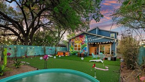 A backyard with a swimming pool, a blue house with a mural, string lights, and outdoor furniture. - Chic 4BR Austin Retreat w/ Cowboy Pool, Hot Tub & Sauna — Near Downtown (Austin)