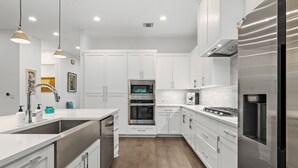 A modern kitchen with white cabinetry, stainless steel appliances, and a wooden floor. - Chic 4BR Austin Retreat w/ Cowboy Pool, Hot Tub & Sauna — Near Downtown (Austin)