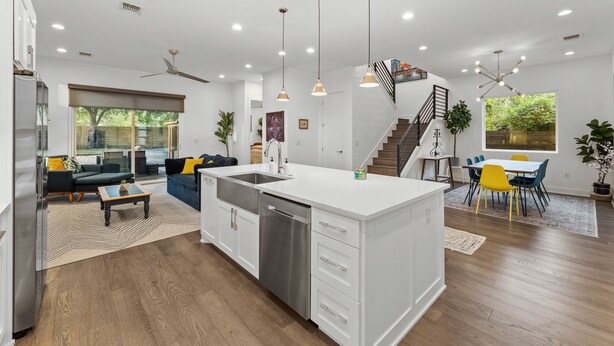 A modern kitchen with a central island, a dining area with yellow chairs, and a staircase leading to another level. - Chic 4BR Austin Retreat w/ Cowboy Pool, Hot Tub & Sauna — Near Downtown (Austin)