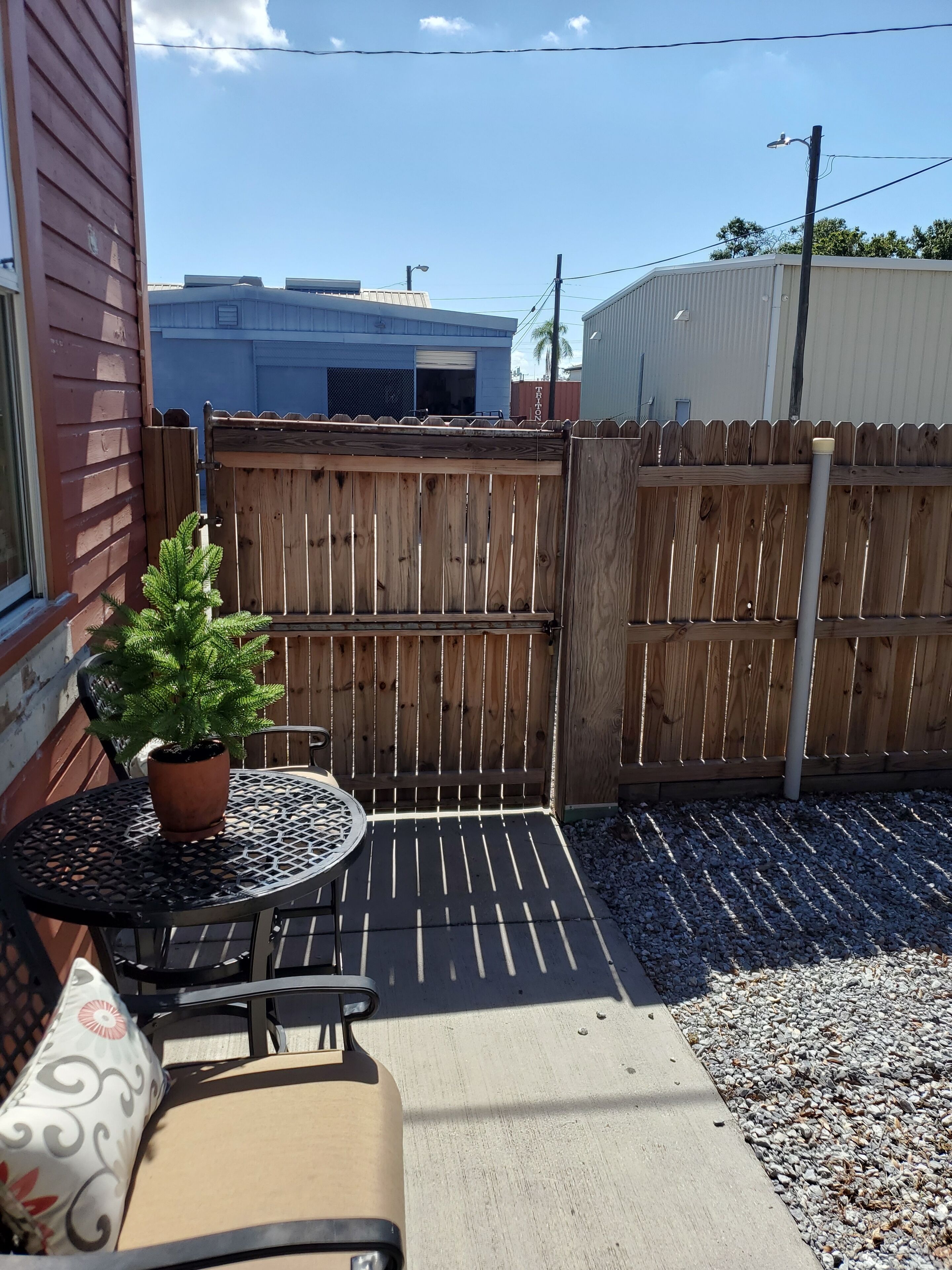 Een terras met een tafel, stoelen, een plant in pot en een houten omheining.
