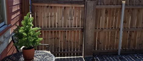 Een terras met een tafel, stoelen, een plant in pot en een houten omheining.