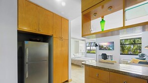 Eine moderne Küche mit Holzausstattung, einem Edelstahlkühlschrank, einer Marmorarbeitsplatte und Meerblick durch große Fenster.