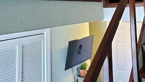 Una escalera con barandilla de madera, un televisor de pantalla plana montado en la pared y una obra de arte con un árbol enmarcado.