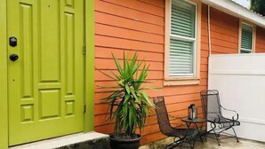 Una casa con una puerta verde brillante, revestimiento naranja y un pequeño patio con una silla y una planta en maceta.