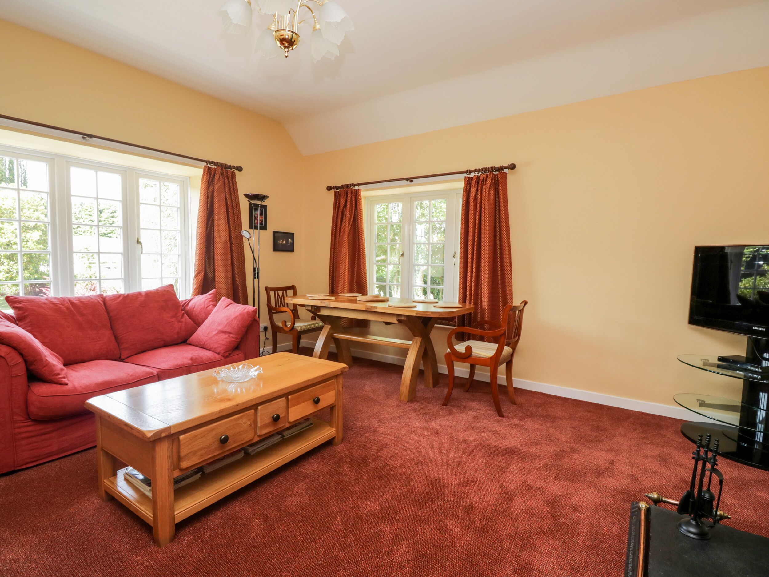 A cozy living room with a red sofa, wooden coffee table, and a dining area with a wooden table and chairs.