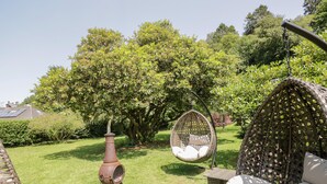 Un jardín con una silla colgante, un sofá de mimbre y una chimenea decorativa.