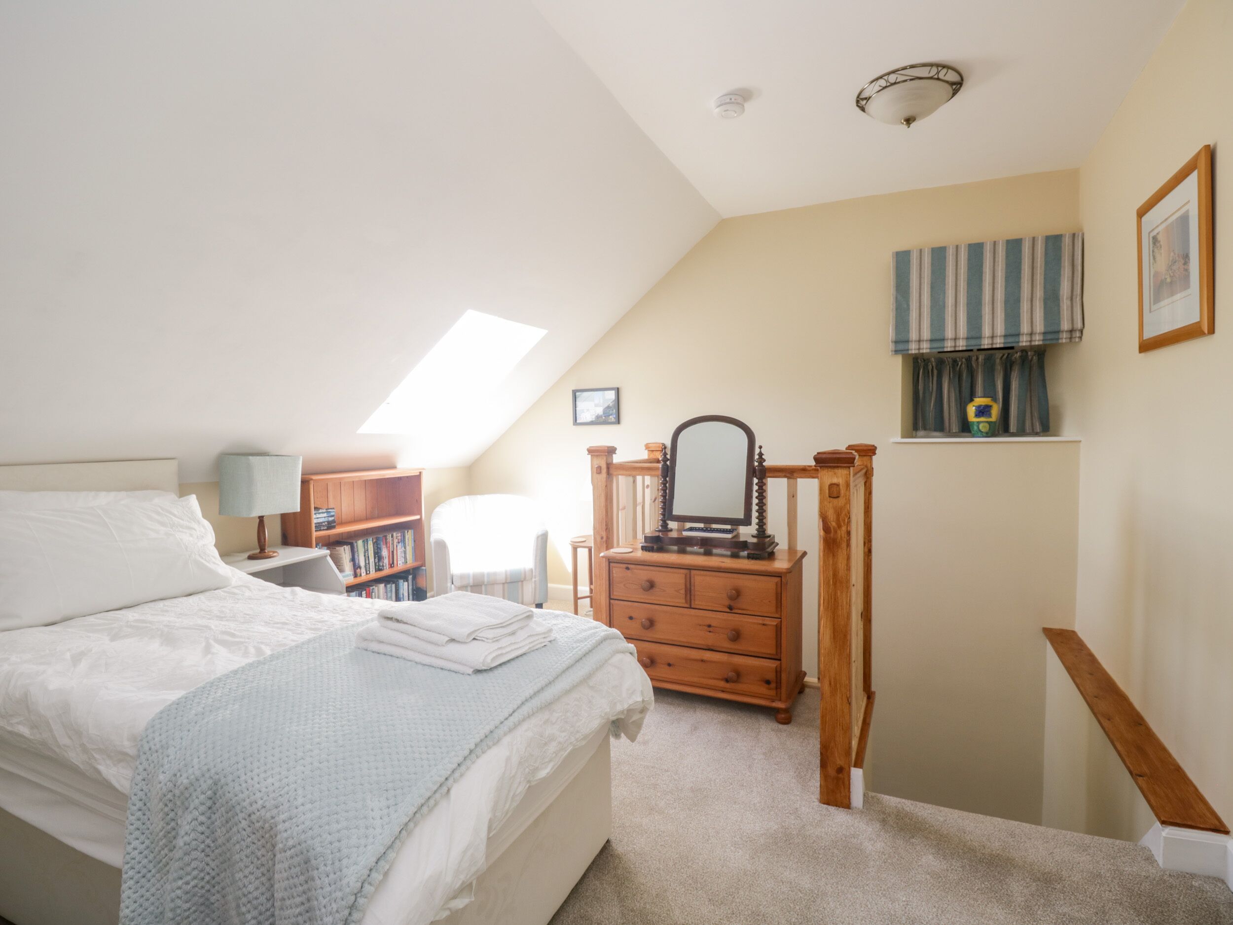 Une chambre à coucher comprenant un lit, une commode, une coiffeuse avec un miroir, une bibliothèque et une fenêtre avec des rideaux.