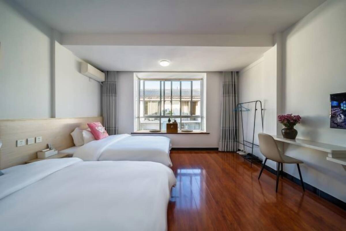 A hotel room with two beds, a desk, a chair, and a large window with curtains.