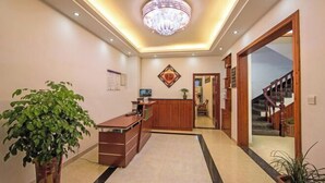 A reception area with a wooden desk, a potted plant, a chandelier, and a staircase. - Mingxuan Inn (Wuyishan)