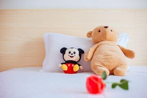 A bed with a white pillow featuring a cartoon character, a plush teddy bear, and a red rose. - Mingxuan Inn (Wuyishan)