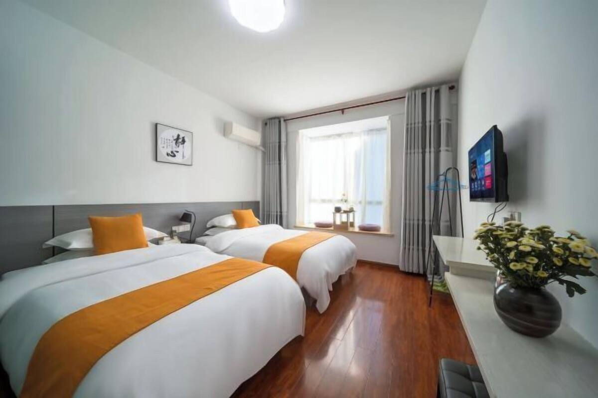 A hotel room with two beds, a desk, a TV, and a window with curtains.