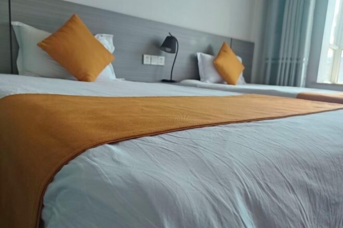 A hotel room with a large bed, two pillows, a bedside lamp, and a window with curtains.