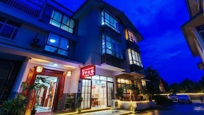 A multi-story building with a prominent red sign at the entrance, large windows, and outdoor seating area with plants. - Mingxuan Inn (Wuyishan)