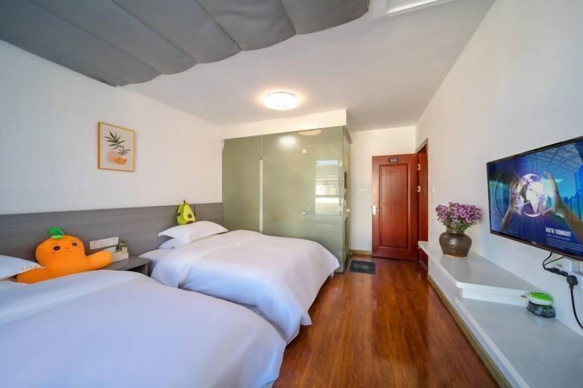 A hotel room with two beds, a television, a door, and a small table with a vase.