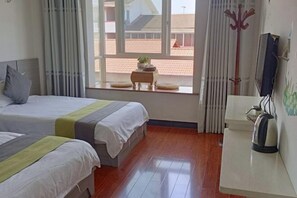 A hotel room with two beds, a small table with a plant, a radiator, and a kettle on a counter. - Mingxuan Inn (Wuyishan)