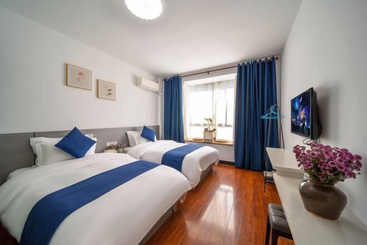 A hotel room with two beds, a TV, a desk, and a window with curtains.