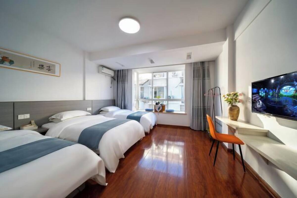 A hotel room with two beds, a TV, a desk, and a window with curtains.