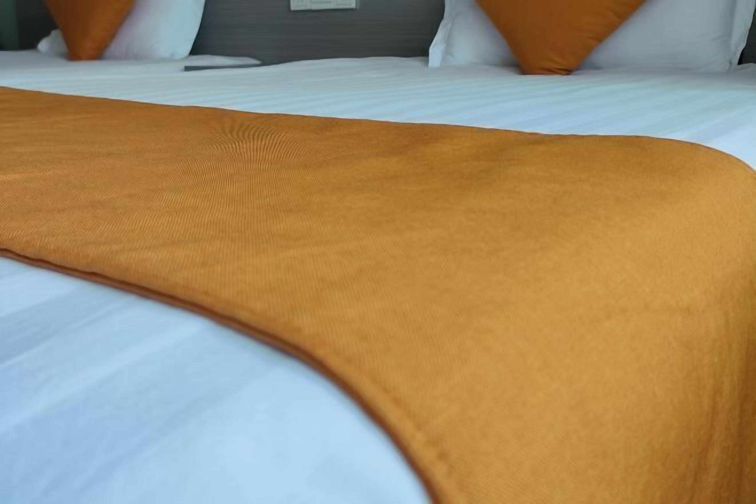 Un lit avec un matelas blanc et une couverture de couleur moutarde.