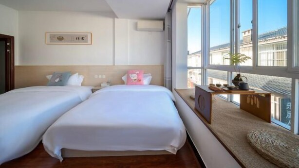 A hotel room with two beds, a large window with a view, and a small table with items on it. - Mingxuan Inn (Wuyishan)