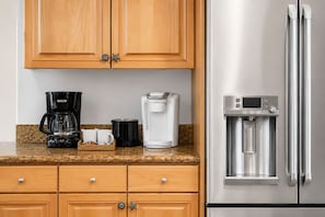 A kitchen with wooden cabinets, a stainless steel refrigerator, a coffee maker, a water dispenser, and a microwave.