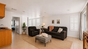 A spacious living area with a sofa, armchair, ottoman, and a small side table with a lamp. - Luxury Beach Mansion - Roof Deck- Steps to Sand (Oxnard)