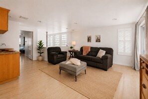 A spacious living area with a sofa, armchair, ottoman, and a small side table with a lamp. - Luxury Beach Mansion - Roof Deck- Steps to Sand (Oxnard)