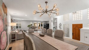 A dining area with a long table, chairs, a chandelier, and a view of the outside. - Luxury Beach Mansion - Roof Deck- Steps to Sand (Oxnard)