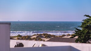 A view of the ocean with waves crashing onto the shore, a distant ship, and some vegetation in the foreground. - Luxury Beach Mansion - Roof Deck- Steps to Sand (Oxnard)