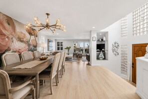 A spacious dining area with a long wooden table, multiple chairs, and a decorative chandelier.