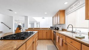 A modern kitchen with wooden cabinets, a granite countertop, a built-in stove, and a large window. - Luxury Beach Mansion - Roof Deck- Steps to Sand (Oxnard)
