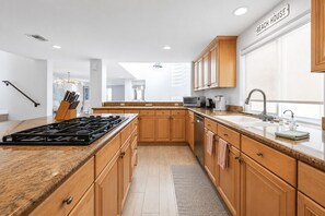 A modern kitchen with wooden cabinets, a granite countertop, a built-in stove, and a large window. - Luxury Beach Mansion - Roof Deck- Steps to Sand (Oxnard)