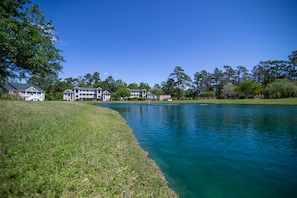 Vista para um lago com área gramada, piscina e vários edifícios com varandas.