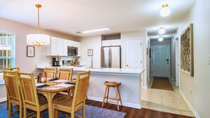 A modern kitchen with white cabinets, stainless steel appliances, and a dining area with wicker chairs and a blue rug.