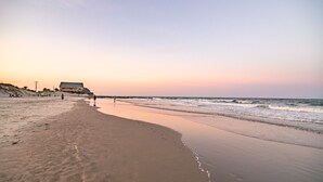 A beach with a building on the left, waves in the distance, and footprints in the sand.