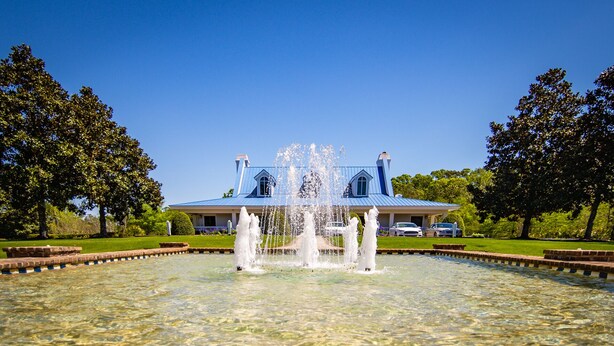A fountain in a clear pool with a house in the background.