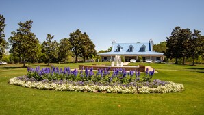 A large house with a blue roof, surrounded by a well-maintained lawn and a circular flower bed with purple and white flowers.