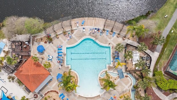 Vue aérienne d’un complexe hôtelier doté d’une piscine centrale, de chaises longues et d’un petit toboggan aquatique.