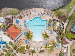 An aerial view of a resort with a central swimming pool, sun loungers, and a small water slide.