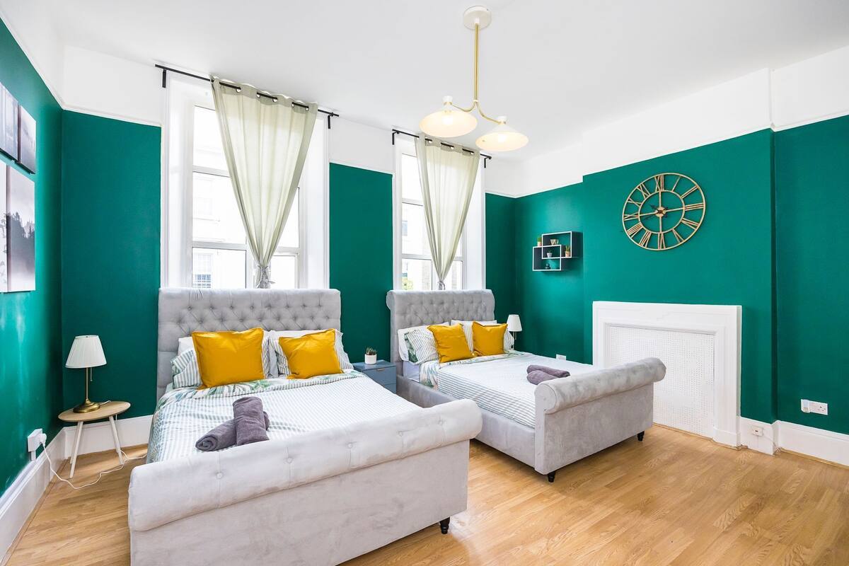 A room with two beds, a white radiator, and a clock on the wall.