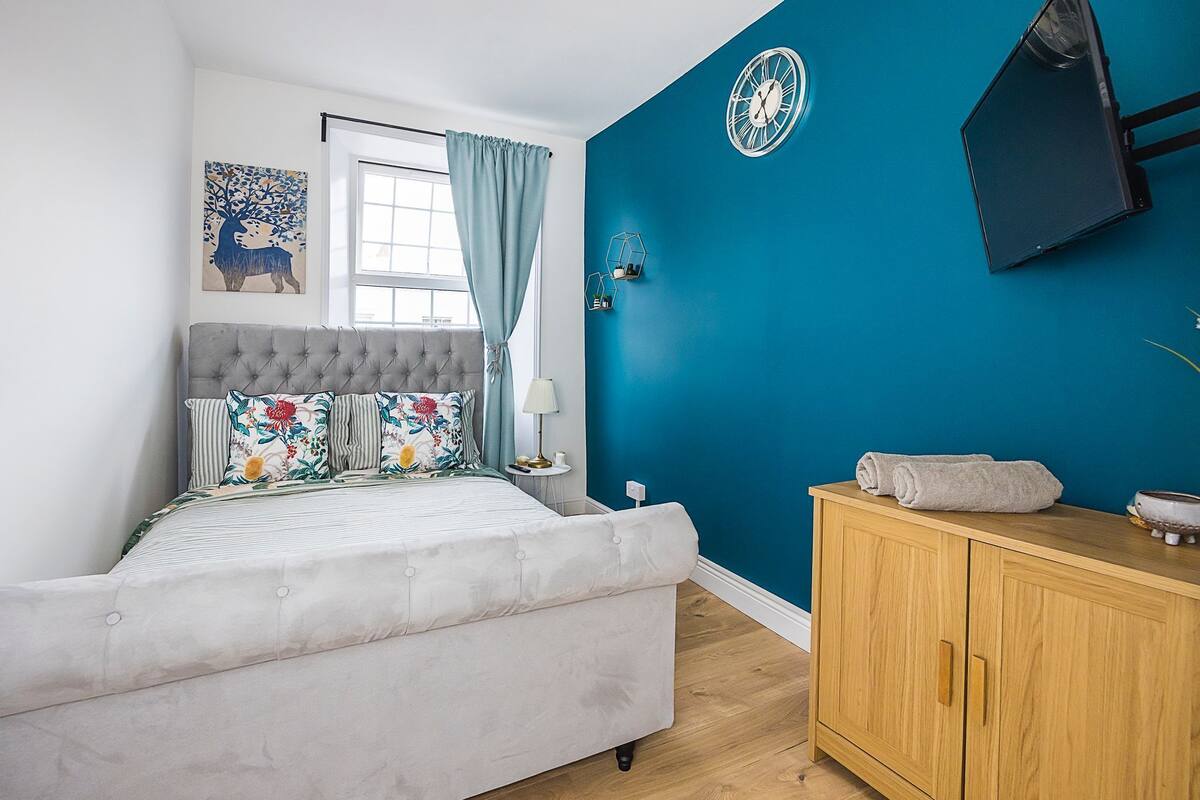A bedroom with a bed, a wooden cabinet, a wall clock, and a window with curtains.