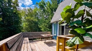 Une terrasse en bois avec un banc et une table, entourée d’arbres et d’un bâtiment.