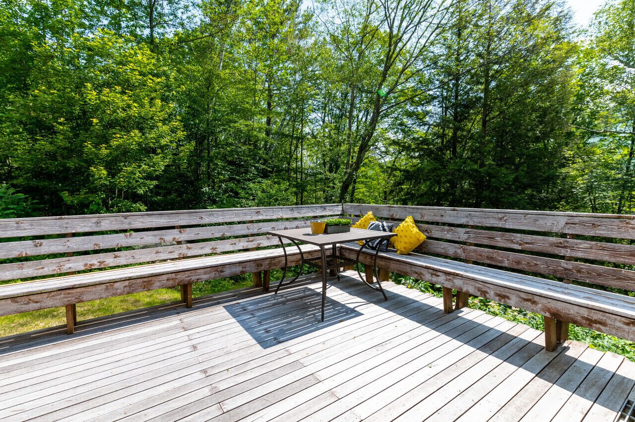 A wooden deck with benches and a table, surrounded by lush greenery.