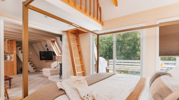Une chambre avec un grand lit, une échelle en bois, une télévision et une vue sur l’extérieur.